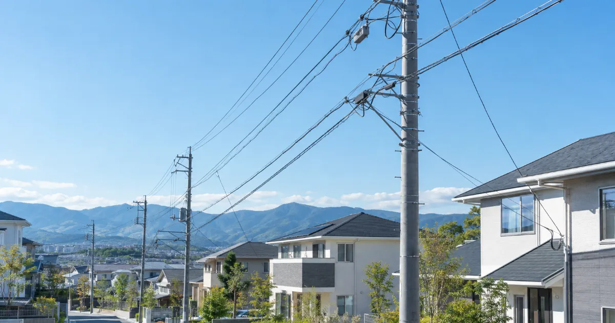 山並みを背にした住宅街の電柱と電線、並んだ戸建て住宅